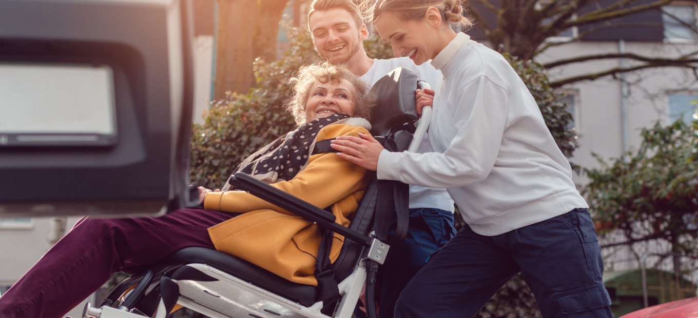 Man and woman assist a woman in a wheelchair to get into an upfitted mobility van