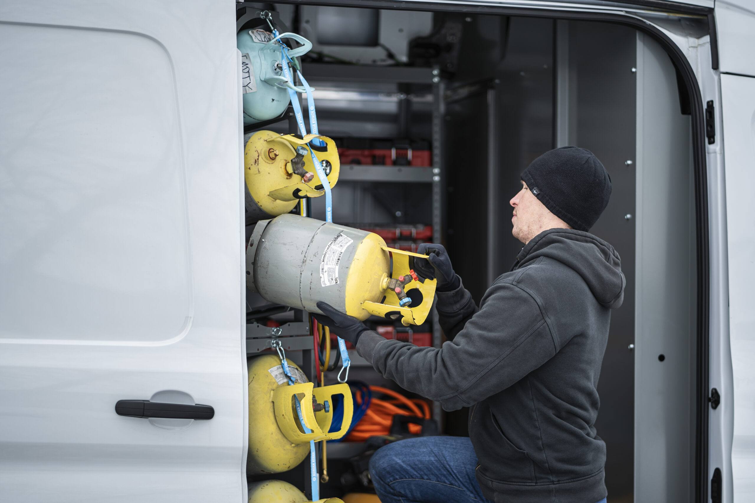 Photo credit to Adrian Steel. Photo of a man pulling out a propane tank from a van that has specialized shelving for contractors, keeps the propane tanks from moving around.