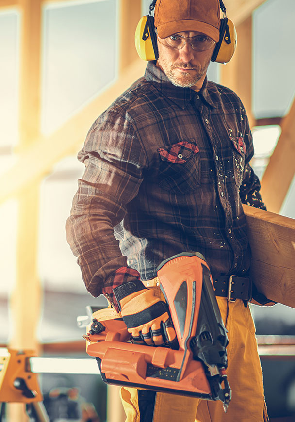Man with nail gun on a construction site looking toward the camera