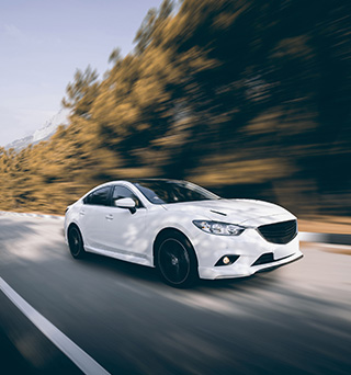 A white sedan driving fast down a rural road