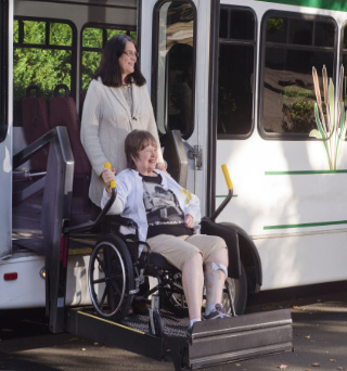 A woman assisting another woman in a wheelchair exiting a handicap upfitted shuttle bus