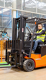 A man driving a forklift wearing a high-vis vest in a manufacturing facility