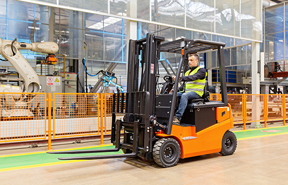 A man driving a forklift wearing a high-vis vest in a manufacturing facility