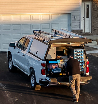 A truck in front of a home upfitted with cabinets in the flatbed cap