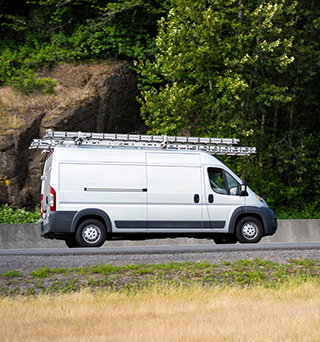 Landscape of a forest with a silver van upfitted with ladder racks