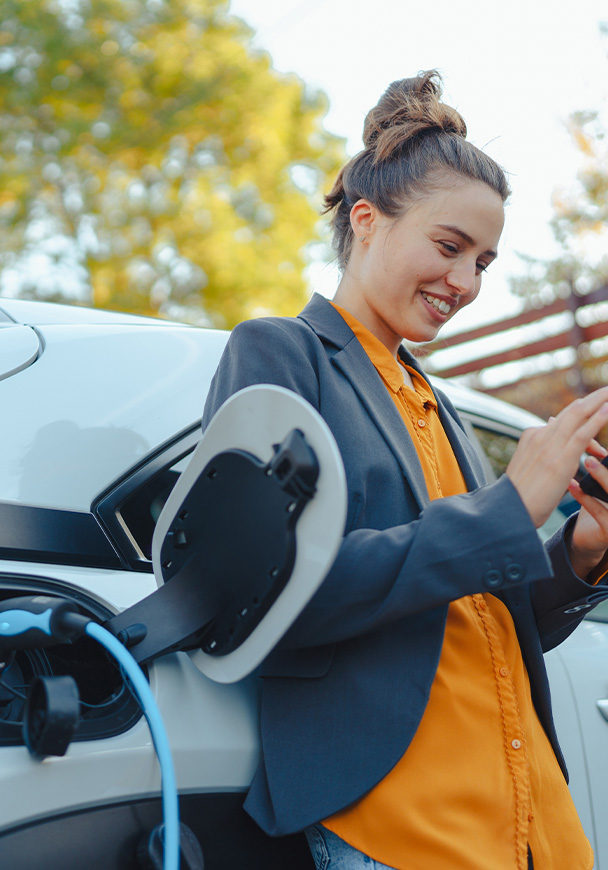 A woman charging her electric vehicle while on her phone