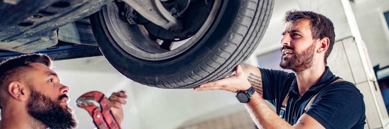 Two mechanics looking at a tire underneath a car. Capital Lease group provides full maintenance services for our leased cars and trucks and leased vans